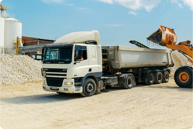 Camião basculante branco a ser carregado por máquina escavadora amarela num estaleiro de construção.