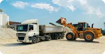 Camião basculante branco a ser carregado por máquina escavadora amarela num estaleiro de construção.